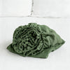 A tightly rolled, olive green linen fitted sheet with deep pockets resting on a white surface.