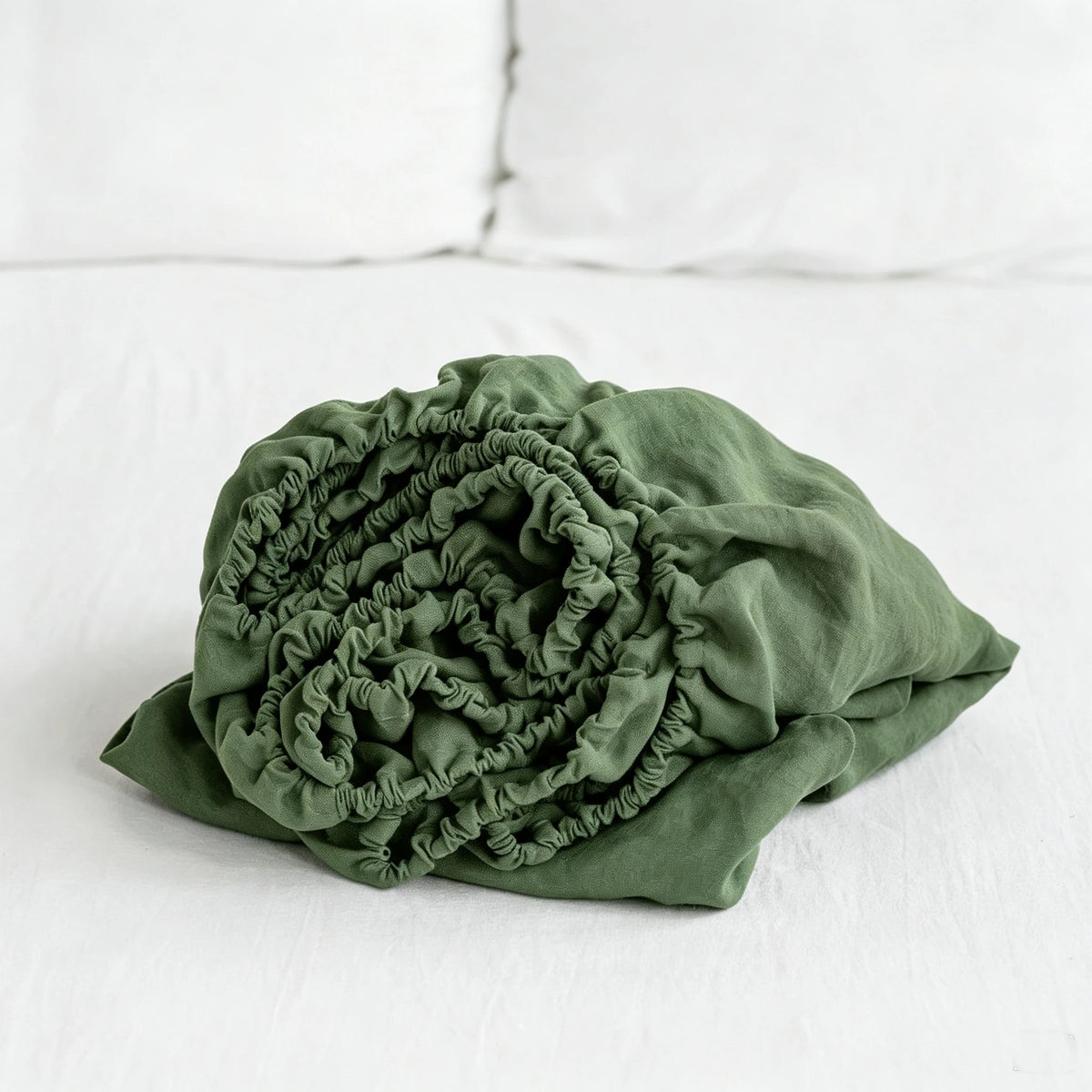 A tightly rolled, olive green linen fitted sheet with deep pockets resting on a white surface.