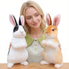 A woman is holding two lifelike plush rabbit stuffed animals, one black and white and one orange.
