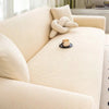 A light beige stretch jacquard sofa cover with a textured fabric and a decorative knitted cushion on a modern sofa.