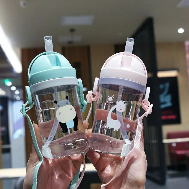 A person holds a clear plastic sippy cup with a gravity straw and a silicone lid in light green and pink colors.