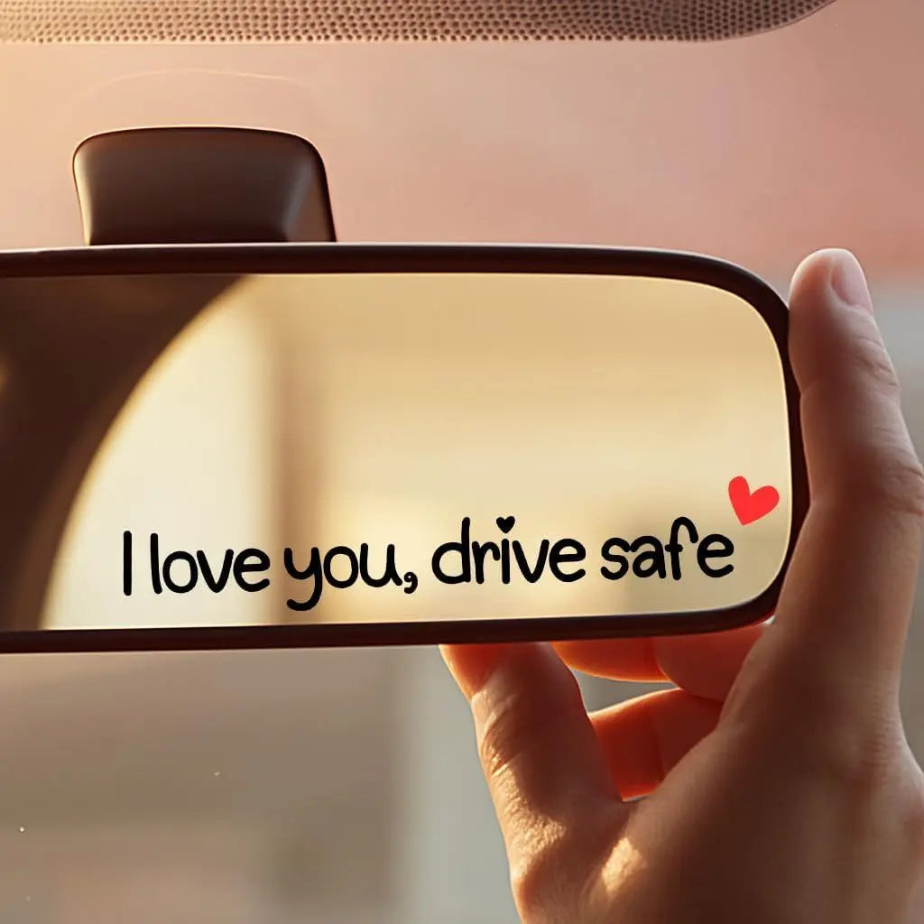 A hand holds a rectangular car decal sticker with the text I love you drive safe on it.