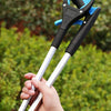 A hand is holding a blue and black foldable reacher grabber tool against a blurred green outdoor background.