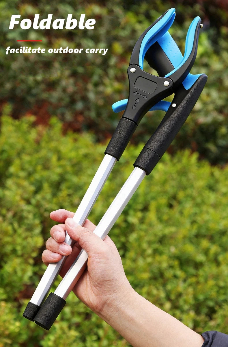 A hand is holding a blue and black foldable reacher grabber tool against a blurred green outdoor background.