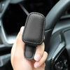 A hand holds a black magnetic leather sunglasses holder designed for car sun visors.