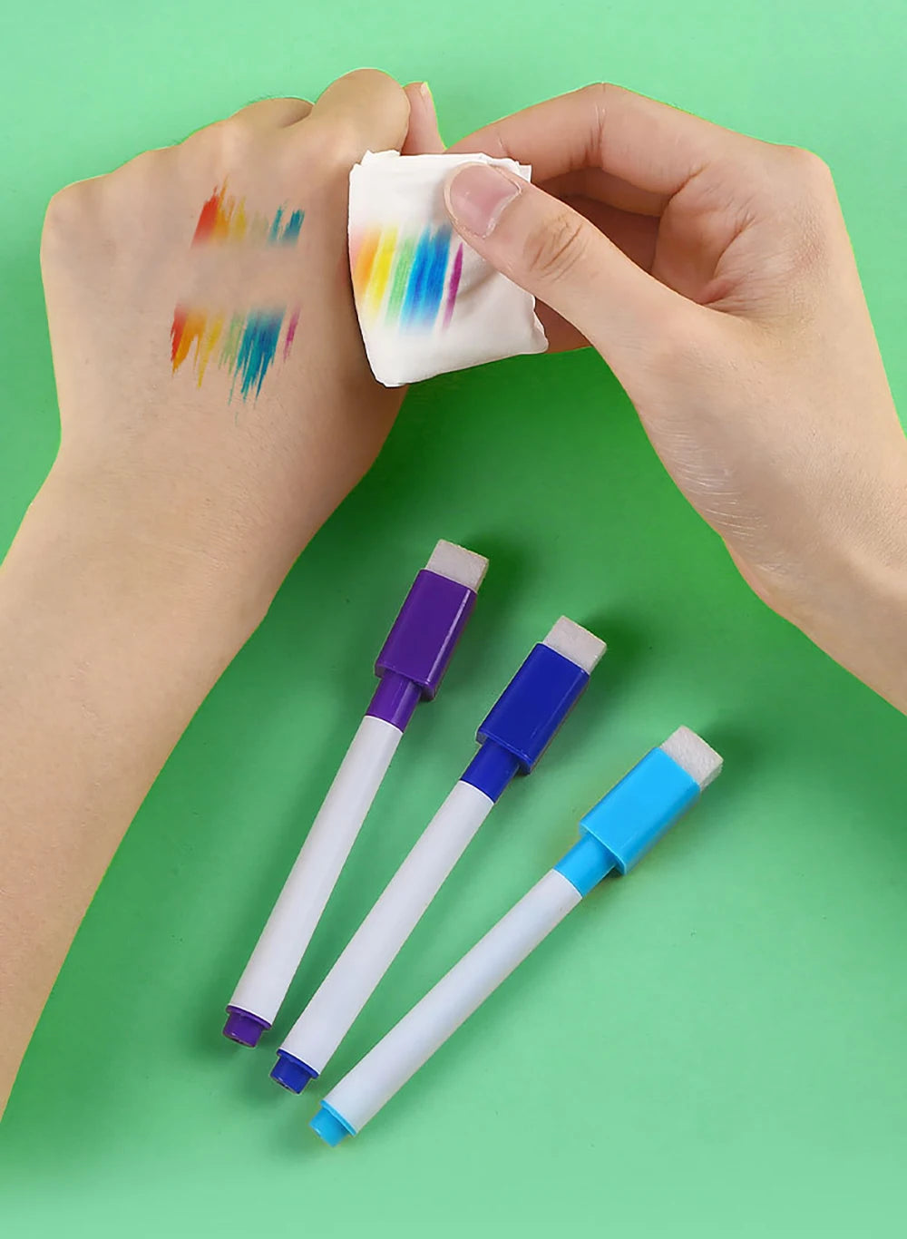 A hand holds a white marker and a piece of paper with colorful paint marks on a green background.