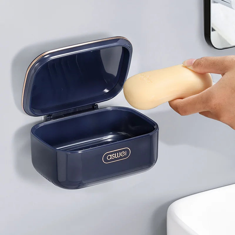 A dark blue two-tier draining soap holder with a lid is shown mounted on a wall next to a yellow bar of soap.