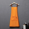 Orange waterproof adjustable kitchen apron hanging on a wooden hanger against a gray wall.