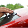 A hand is applying a black rubber seal strip to the edge of a red car window or sunroof.