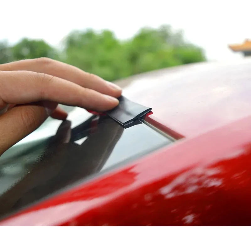A hand is applying a black rubber seal strip to the edge of a red car window or sunroof.
