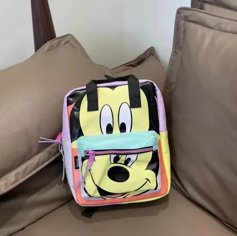 A yellow and black cow print backpack with pink trim resting on a beige sofa cushion.