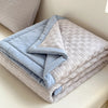 A stack of light blue and gray breathable waffle-weave summer quilts folded on a white surface.