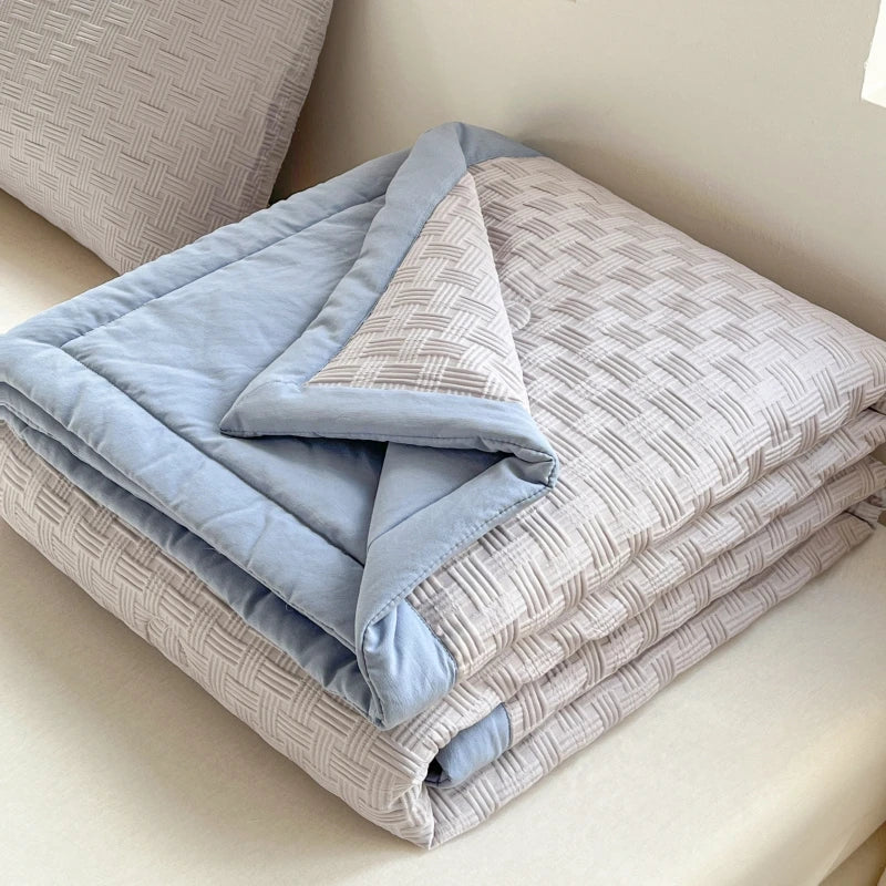 A stack of light blue and gray breathable waffle-weave summer quilts folded on a white surface.
