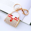 A gold-toned handbag keychain featuring a white and red striped design adorned with crystal rhinestones.
