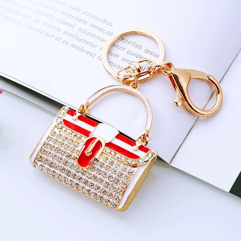 A gold-toned handbag keychain featuring a white and red striped design adorned with crystal rhinestones.