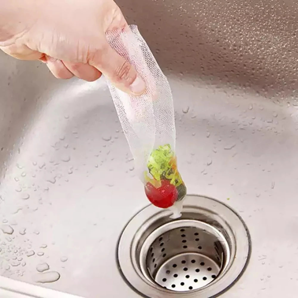 A hand is placing a small piece of fruit into a disposable mesh sink strainer bag over a kitchen sink drain.