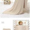 A beige soft cotton baby blanket draped on a table, next to a folded blanket and a child using it.
