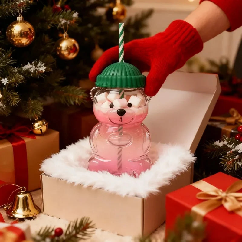يد ترتدي قفازًا أحمر تحمل كوبًا على شكل دب وردي بعصا مخططة في صندوق أبيض محاط بالفرو الأبيض.