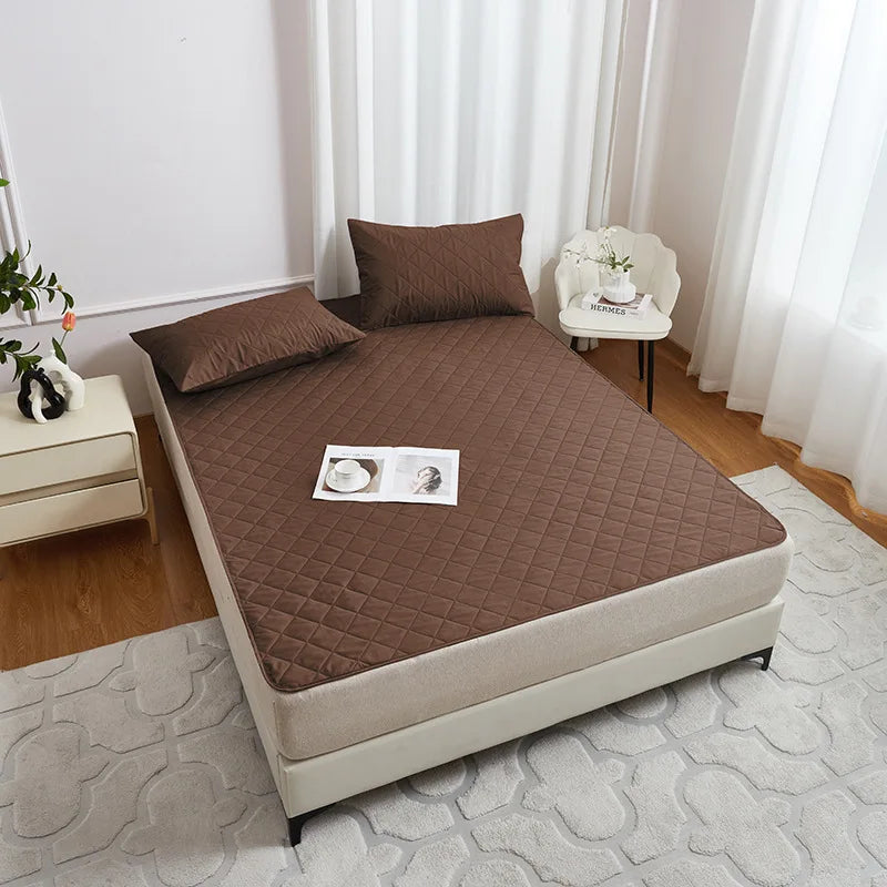 A brown waterproof mattress protector with elastic straps is displayed on a bed, next to a white chair and a light-colored be
