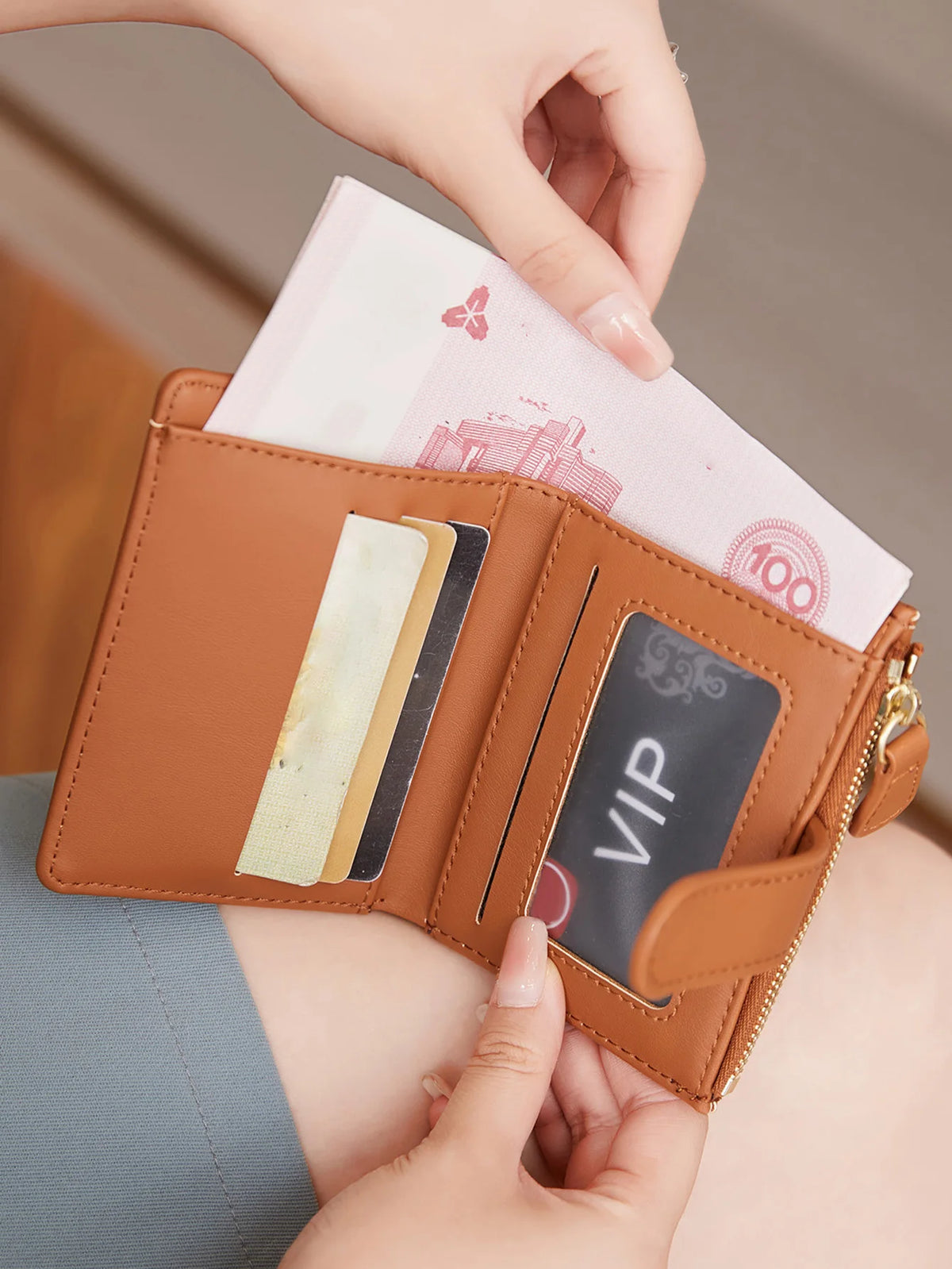 A hand is opening a brown leather bi-fold wallet showing various cards and a pink paper bill.