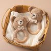 A handmade crochet bunny rattle featuring a natural wood teether ring, resting in a woven basket.