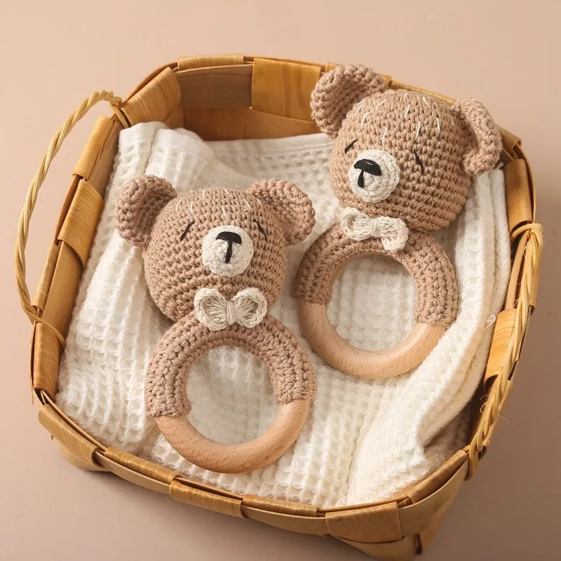 A handmade crochet bunny rattle featuring a natural wood teether ring, resting in a woven basket.
