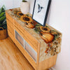 A wooden cabinet with an autumn harvest table runner featuring sunflowers and pumpkins.