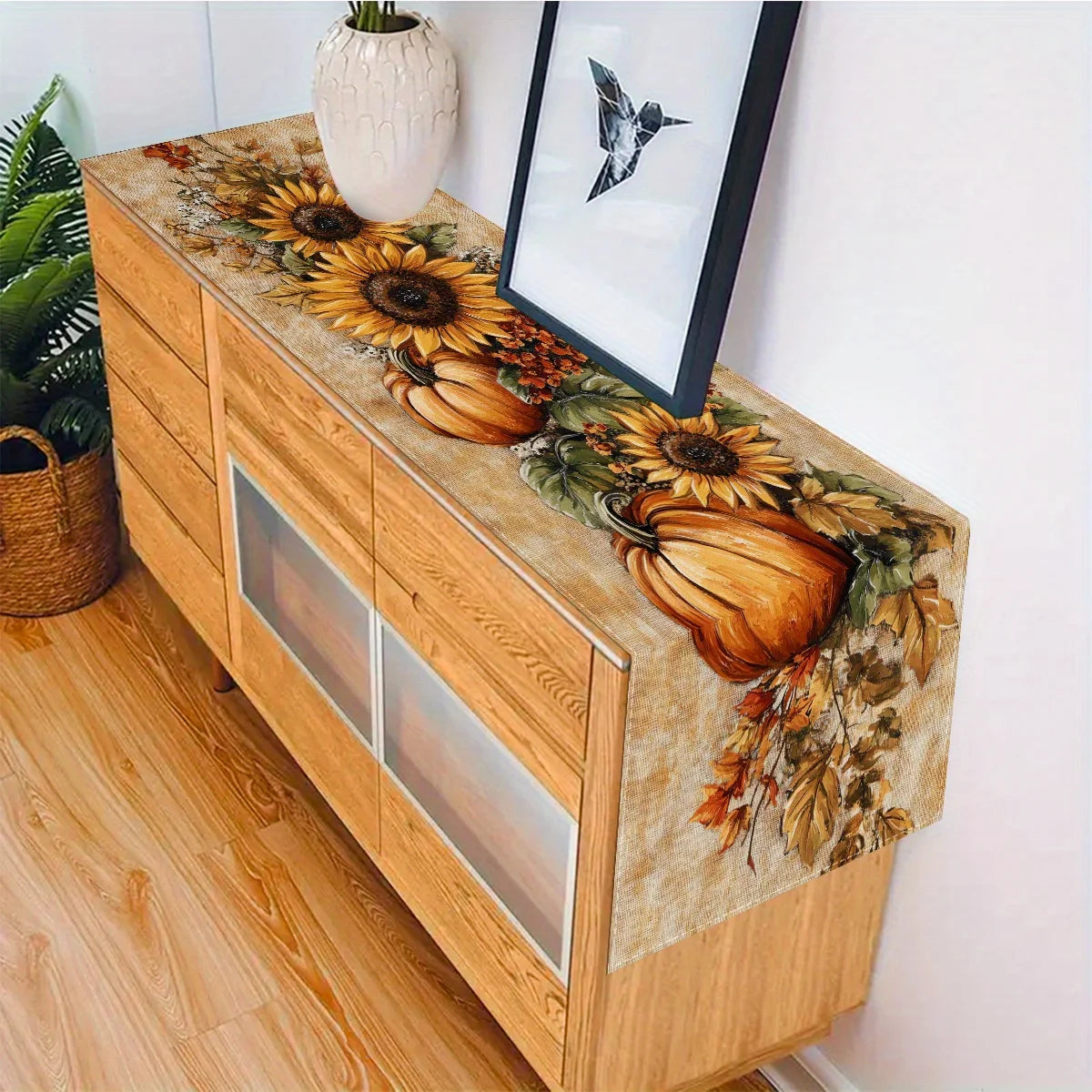 A wooden cabinet with an autumn harvest table runner featuring sunflowers and pumpkins.