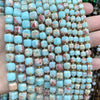 A hand holds a strand of square faceted beads made from natural stone in shades of light blue and pink.