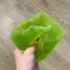 A hand is squeezing a bright lime green, translucent stress ball shaped like a cheese slice.