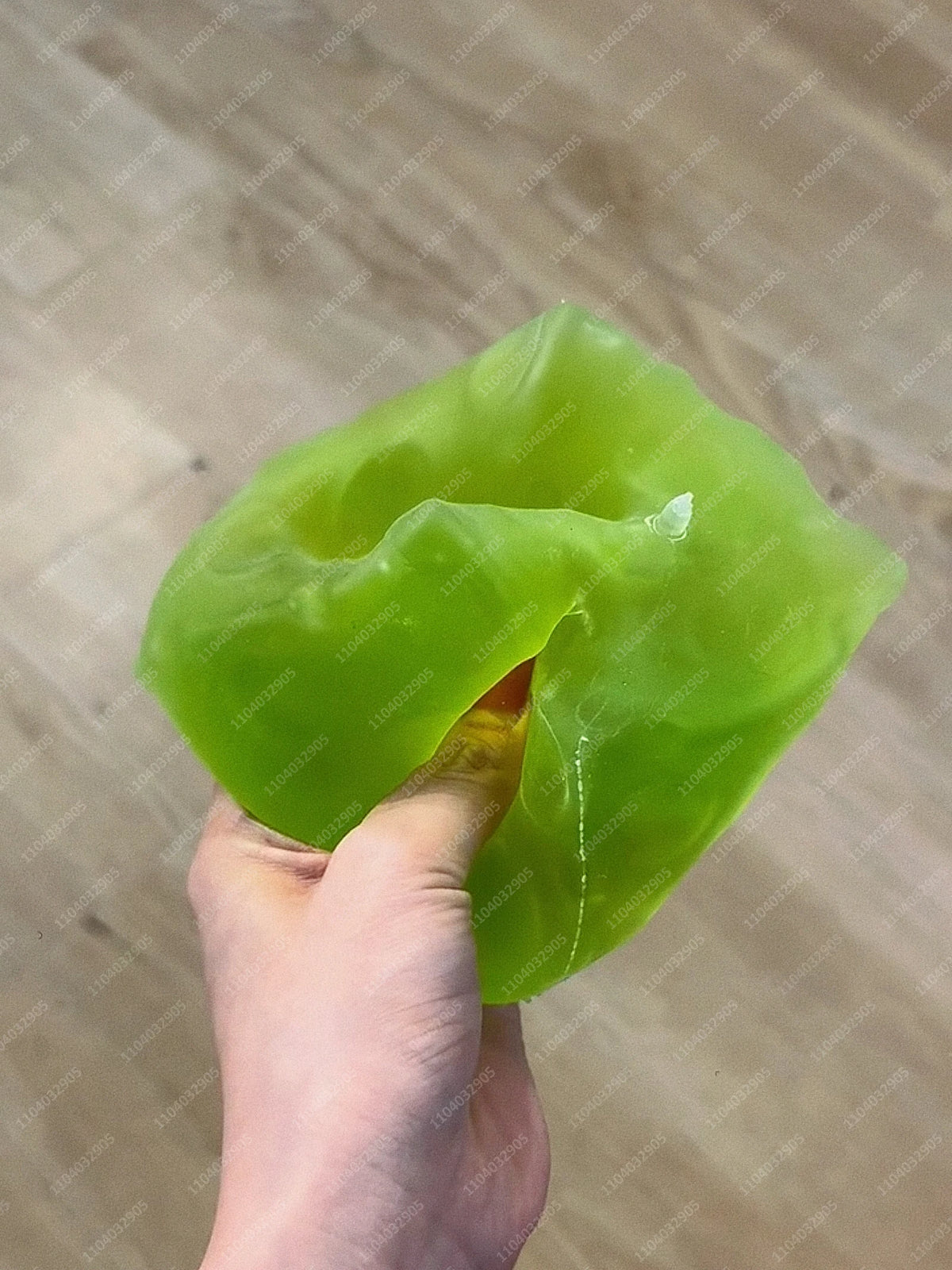 A hand is squeezing a bright lime green, translucent stress ball shaped like a cheese slice.