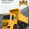 A yellow dump truck is shown with a remote control controller in the foreground against a rocky background.