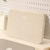 Una funda protectora delgada beige para laptop, mostrada sobre fondo blanco.