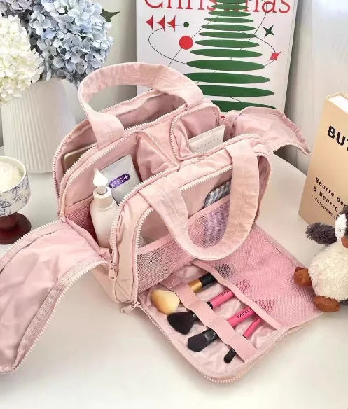 A pink travel makeup bag with a wide opening is shown, containing various cosmetics and tools.
