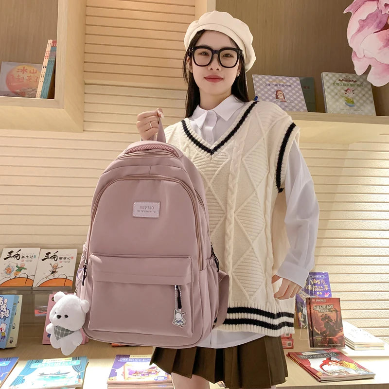 A young woman models a pink waterproof nylon laptop backpack over her shoulder in a bright indoor setting.