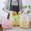 A person wearing an apron holds several mini fruit-print tote bags in pink, green, and yellow colors.