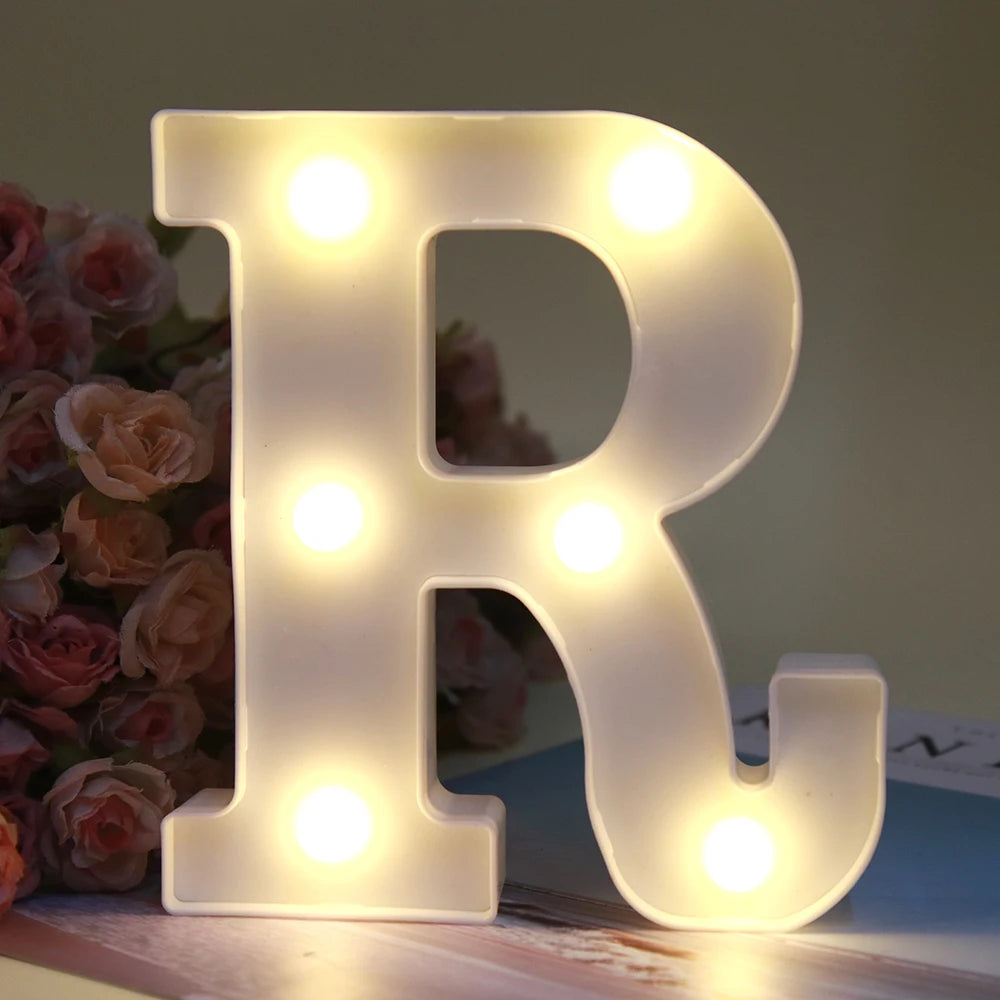 Lettre alphabet R lumineuse blanche LED, veilleuse, posée sur une surface en bois à côté de roses.