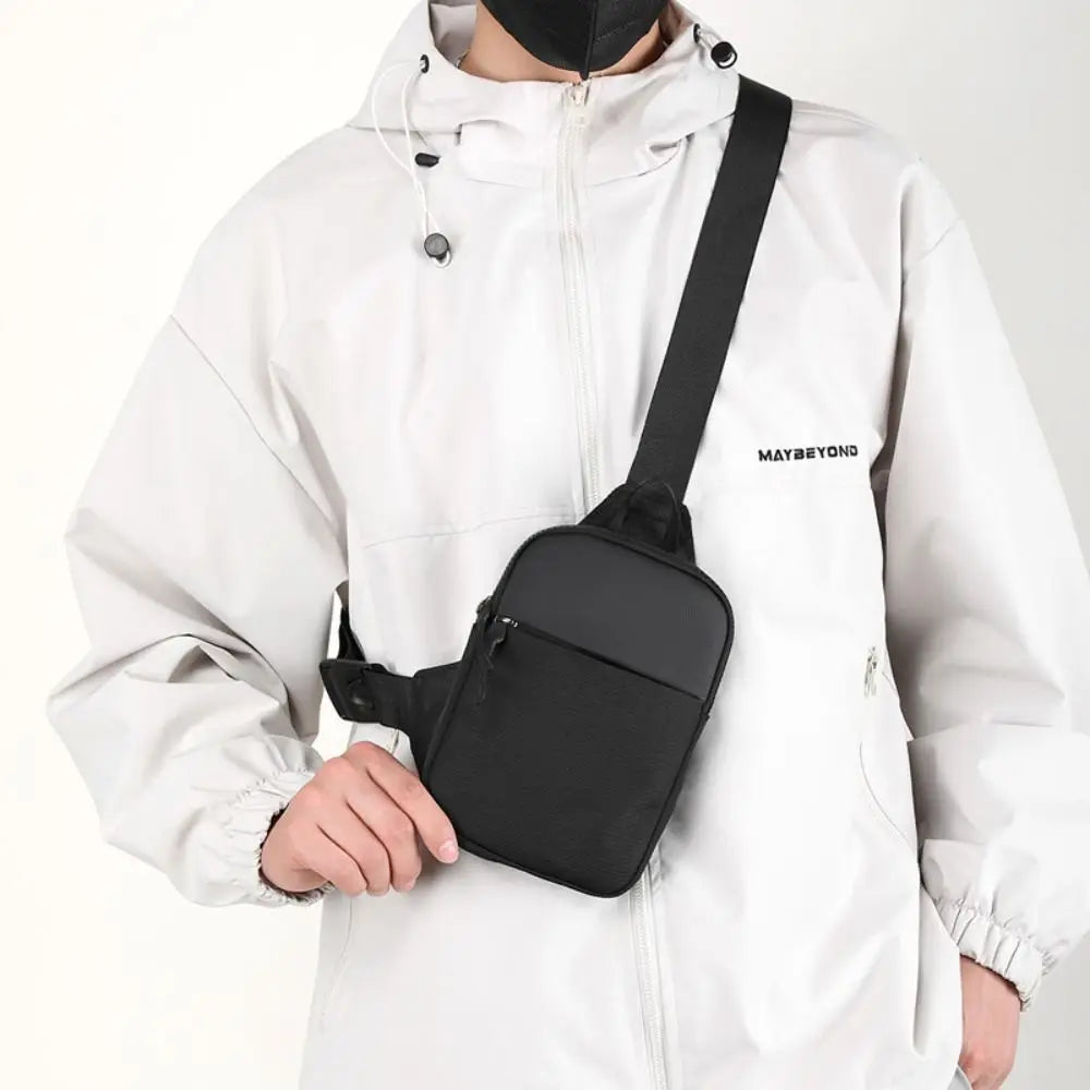 A person wearing a white hooded jacket is holding a black compact canvas crossbody sling bag.
