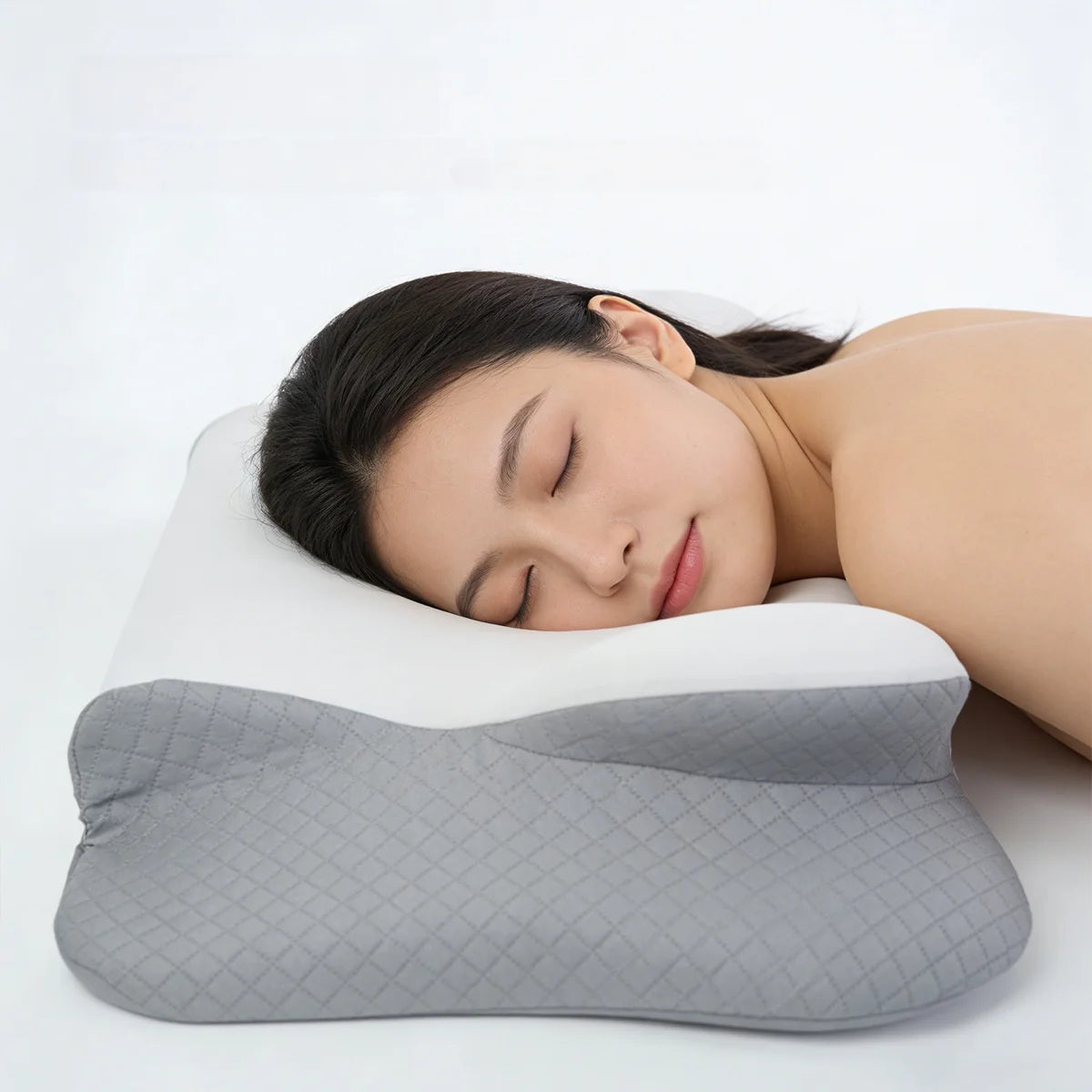 A woman is sleeping comfortably on a gray memory foam pillow for neck pain relief.