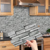 A hand holds a rectangular piece of peel-and-stick tile stickers designed for kitchen and bathroom backsplashes.