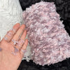 A hand is holding a skein of light purple and white variegated cotton blend yarn for knitting and crochet.