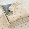 A stack of light beige and gray cartoon patterned kids lightweight summer quilts on a white quilted surface.