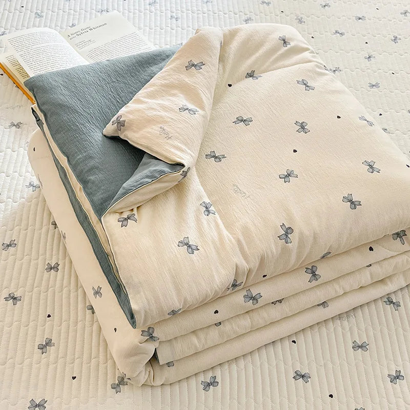 A stack of light beige and gray cartoon patterned kids lightweight summer quilts on a white quilted surface.