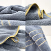 A close-up of a gray fluffy bath towel with gold trim and stitching.