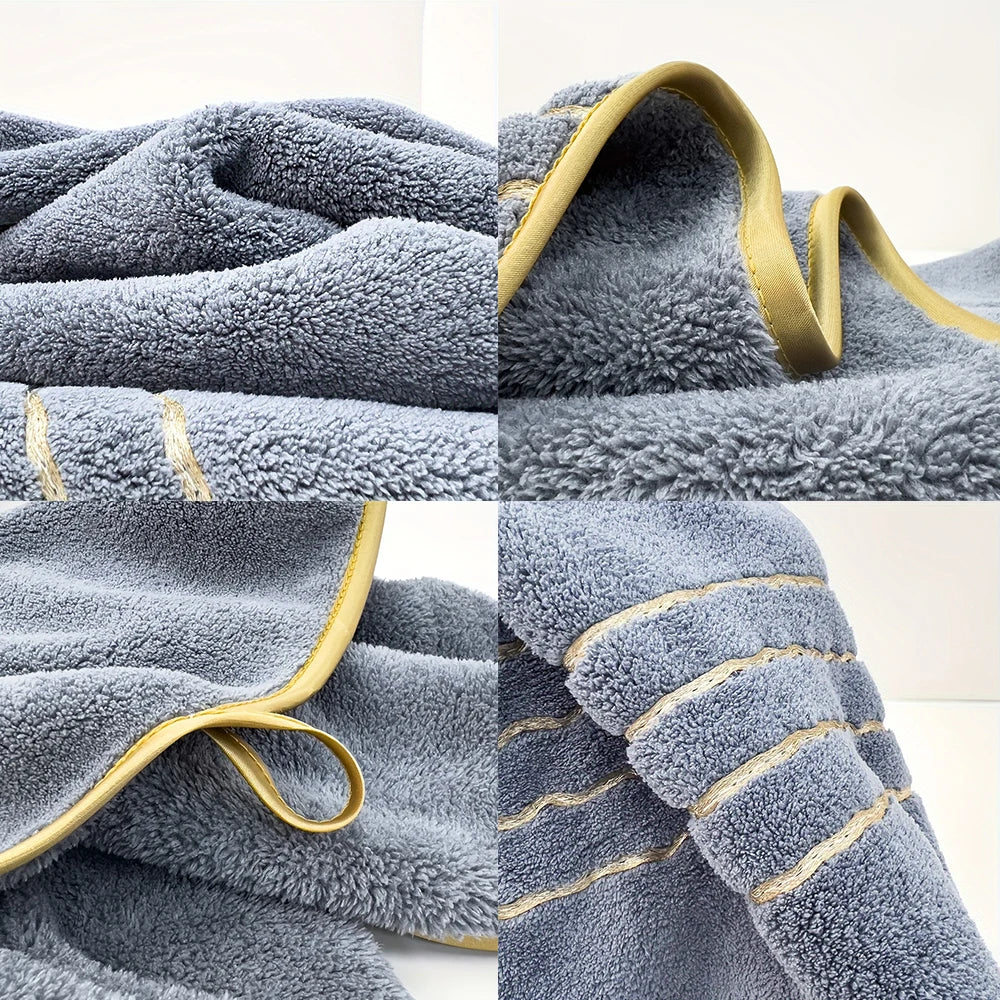 A close-up of a gray fluffy bath towel with gold trim and stitching.