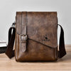 A brown vintage PU leather messenger bag for men with an adjustable strap resting on a wooden surface.