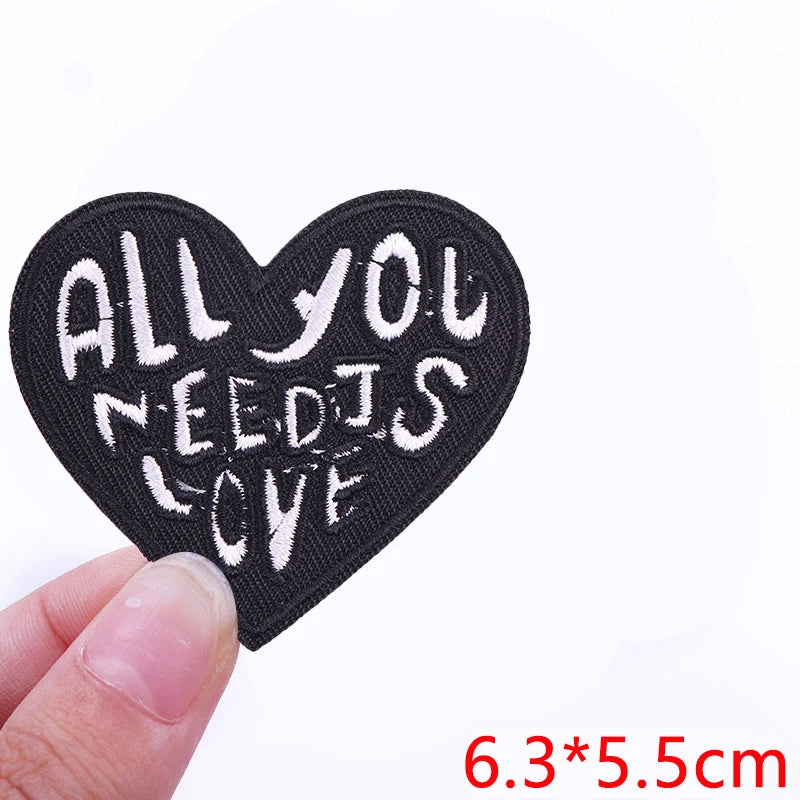Black heart shaped iron-on letter patch embroidered with the text All you need is love