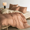 A luxurious rose gold duvet cover set with soft folds on a bed, next to a table lamp.