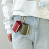 A close-up of a red and olive green retractable keychain tote bag folded into a compact pouch attached to a white sweatshirt 