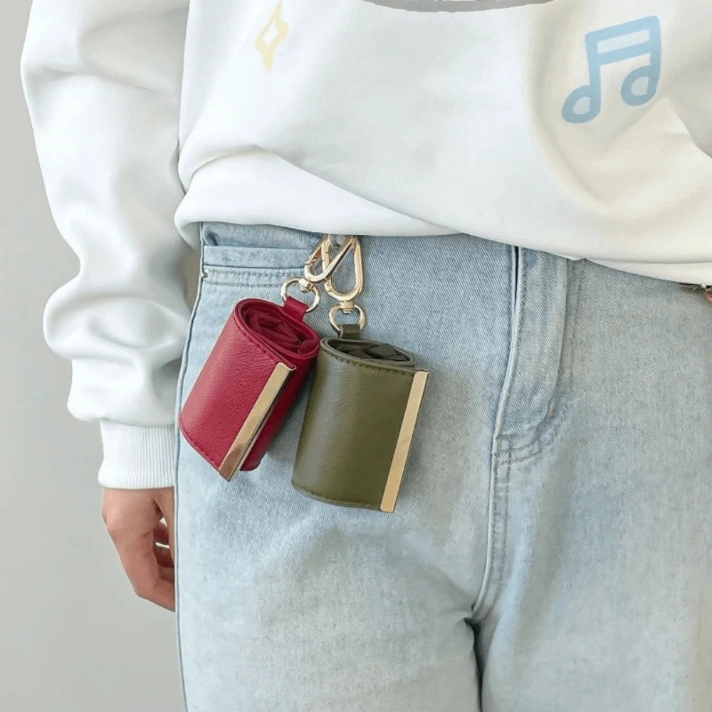 A close-up of a red and olive green retractable keychain tote bag folded into a compact pouch attached to a white sweatshirt 